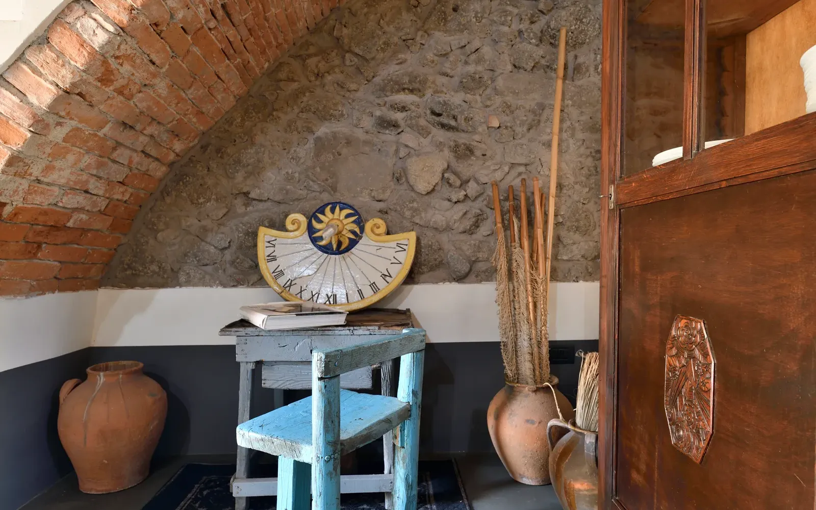 Sotto l’arco: sgabello azzurro, sole di ceramica e brocche in terracotta