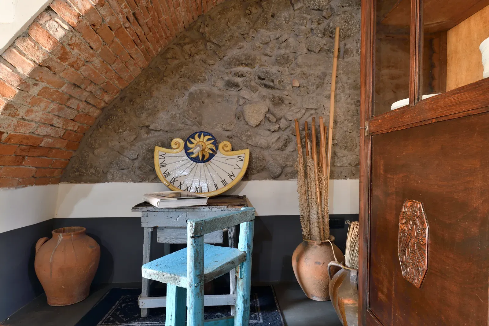 Sotto l’arco: sgabello azzurro, sole di ceramica e brocche in terracotta